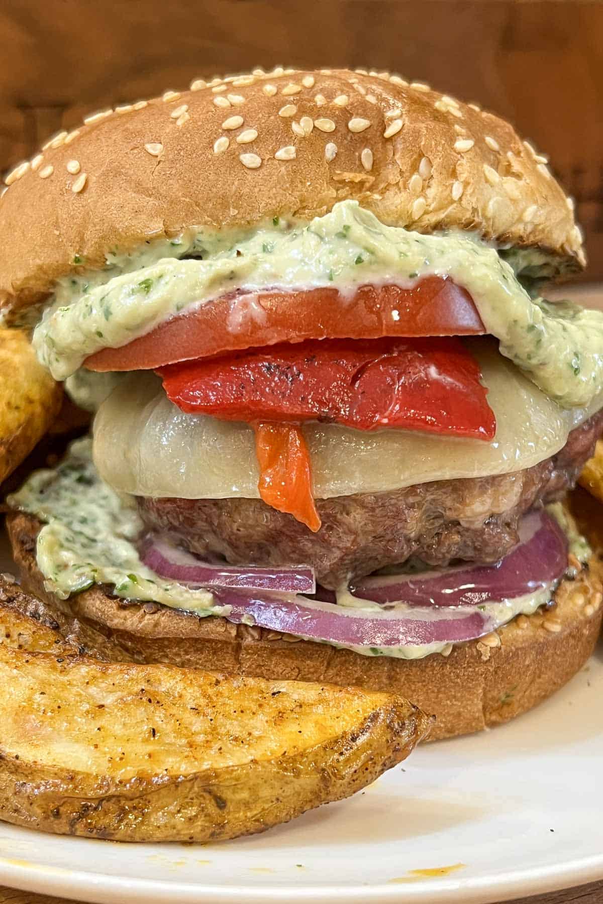 An Italian Burger on a toasted bun layered with basil pesto aioli, red onion, provolone, roasted red peppers and tomato.