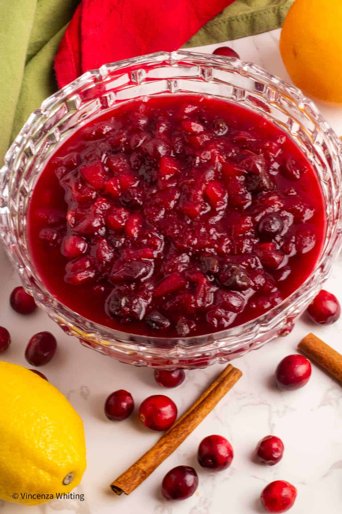 A bowl of Cranberry chutney surrounded by whole cranberries, cinnamon sticks and lemons.