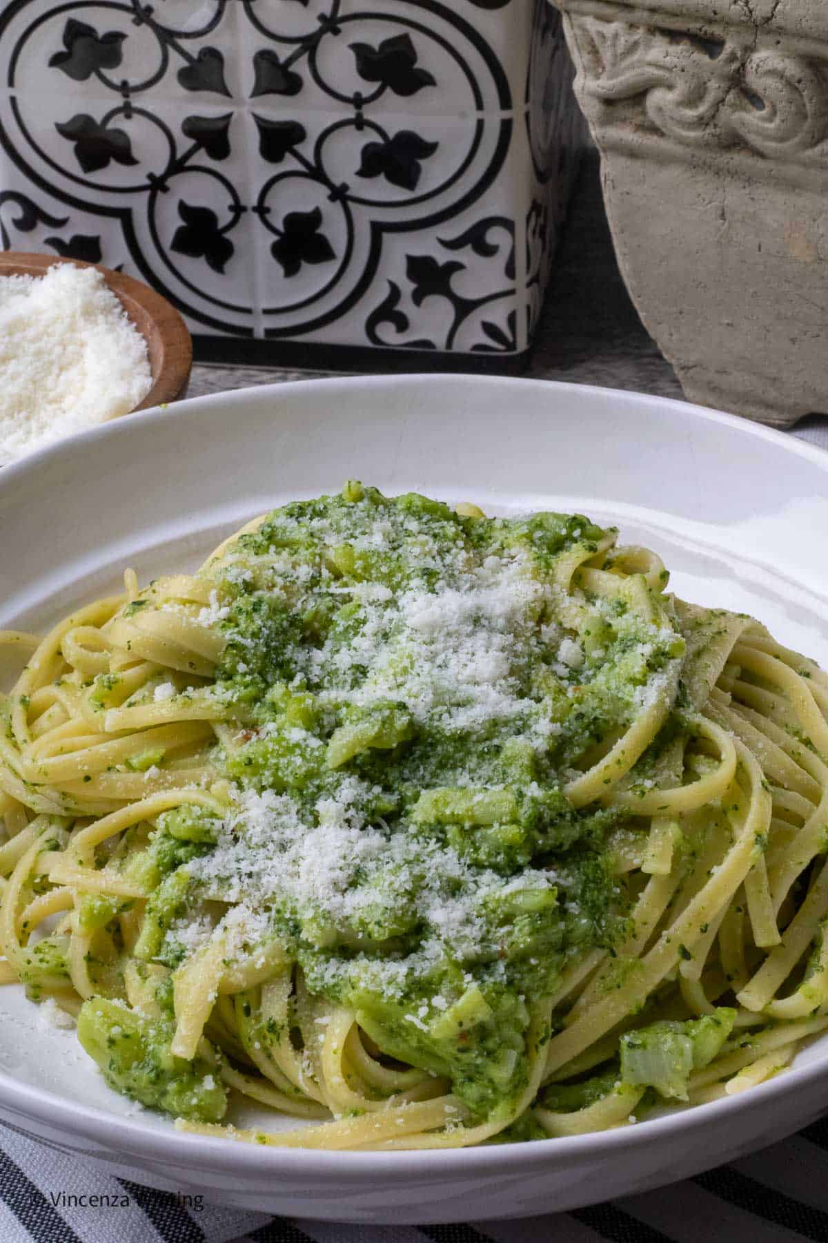 A white bowl of pasta broccoli topped with grated cheese.