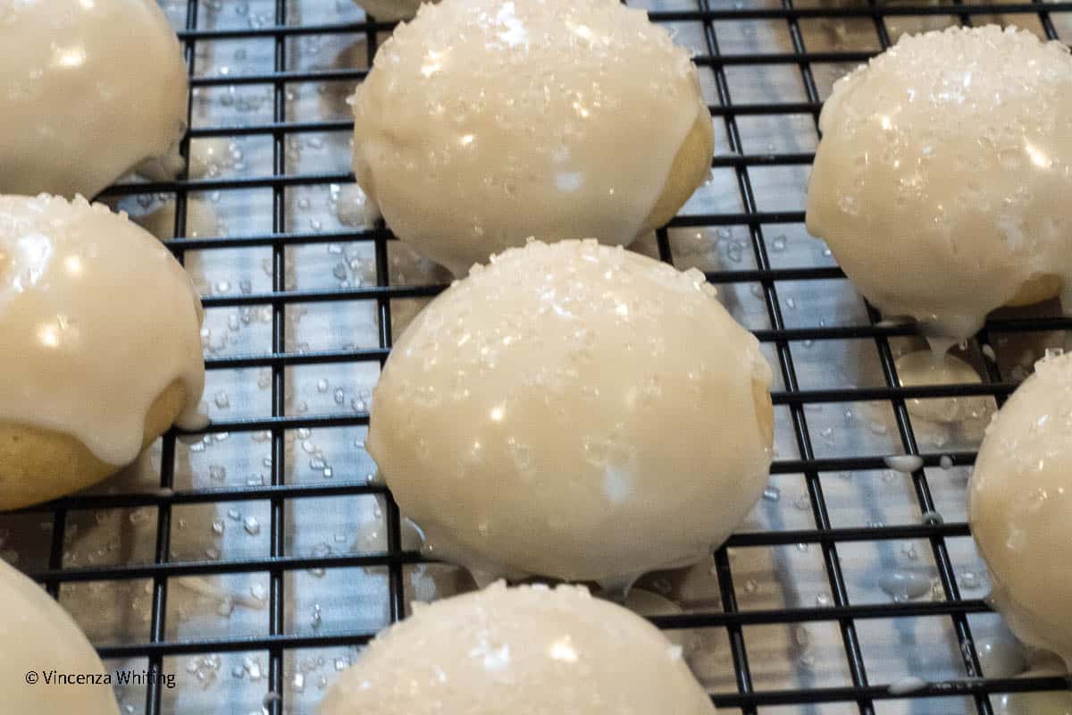 * Anginetti cookies, white domed cookies covered in white icing and sanding sugar drying on a black rack.