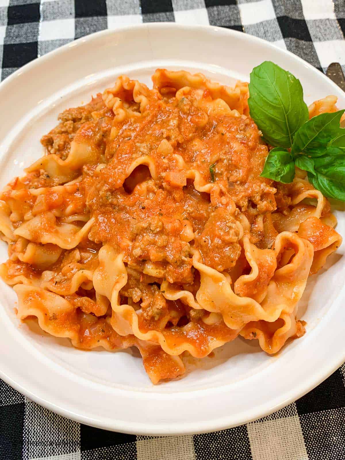 A white bowl of pasta with red meat sauce on a black and white checked cloth.