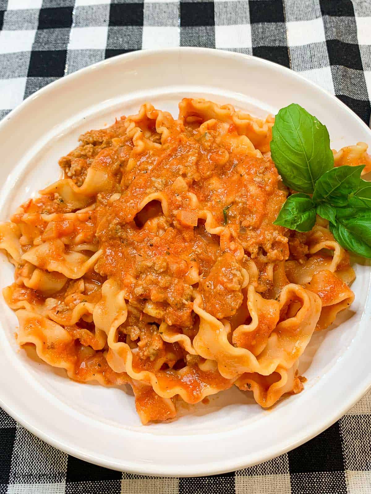 A bowl of pasta with meat sauce on a black and white checked tablecloth.