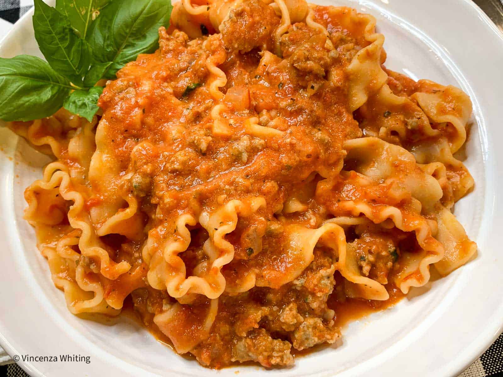 A white bowl of pasta with meat and tomato sauce.