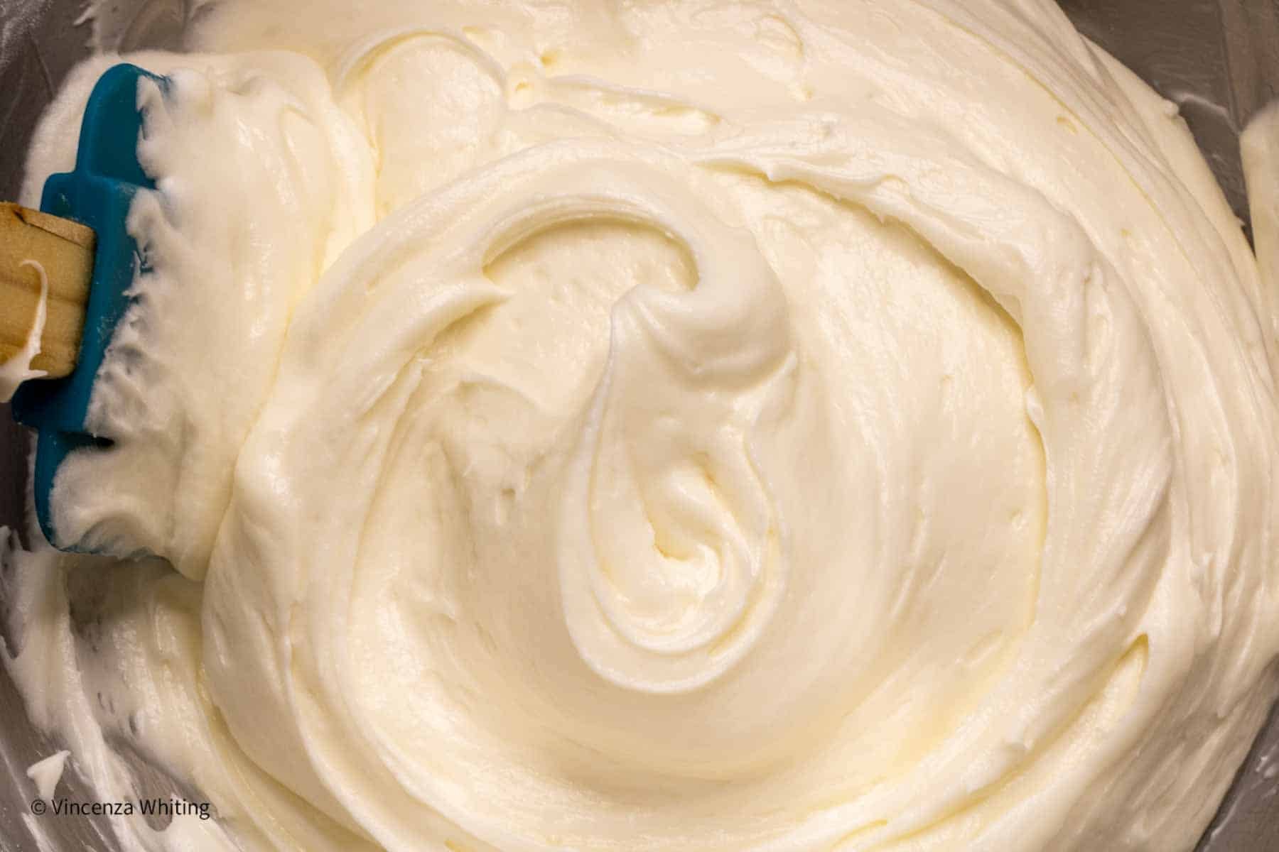 Whipped cream cheese frosting in a bowl with a spatula.