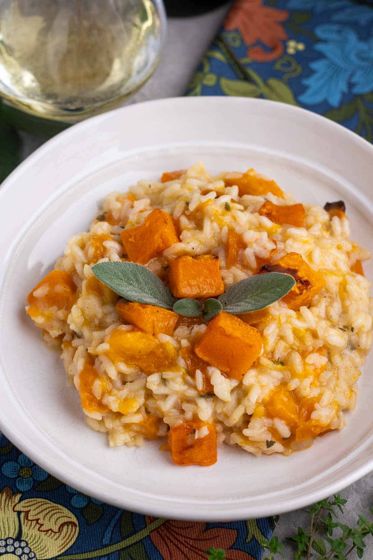 A bowl of butternut squash risotto next to a glass of white wine.   