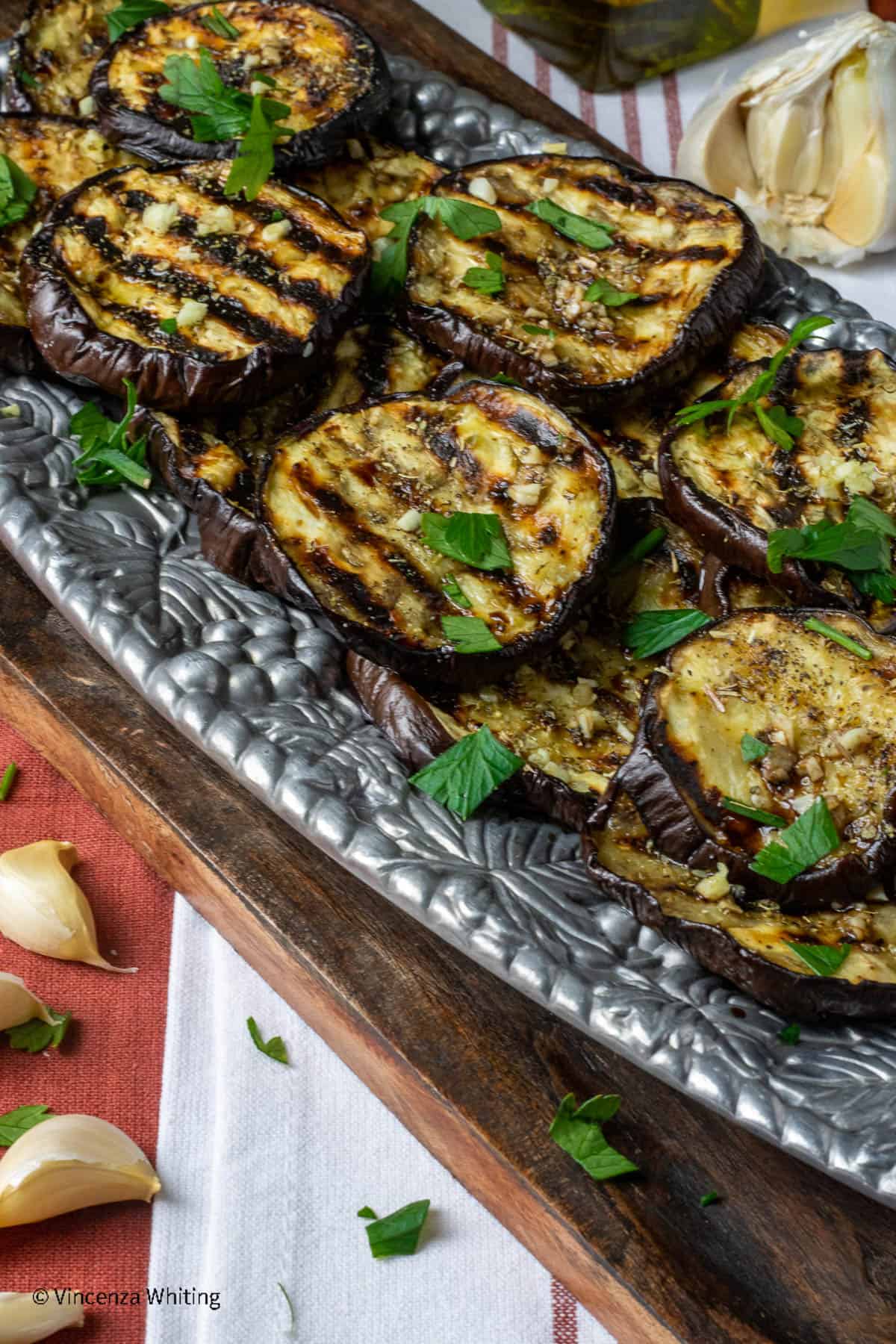 A silver tray of grilled eggplant slices on a red and white cloth.