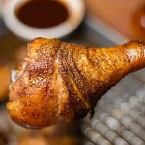 A smoked tureky drumstick in front of a samll bowl of BBQ sauce.