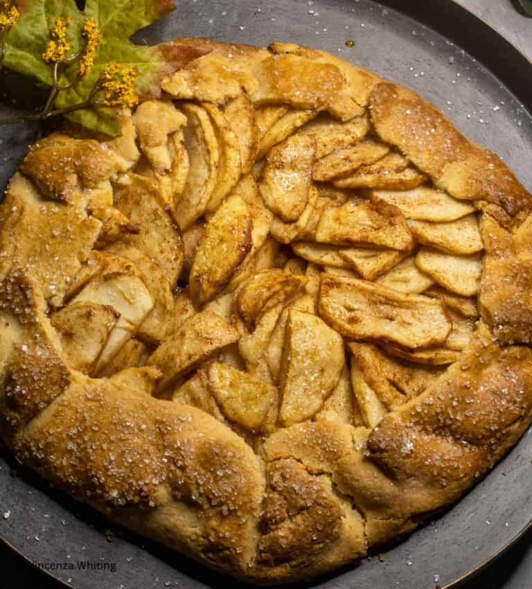 A golden brown rustic apple crostata on a dark metal plate.