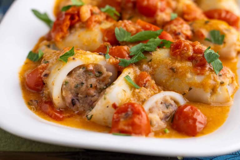 Stuffed calamari on a lwhite plate with tomatoes and parsley.