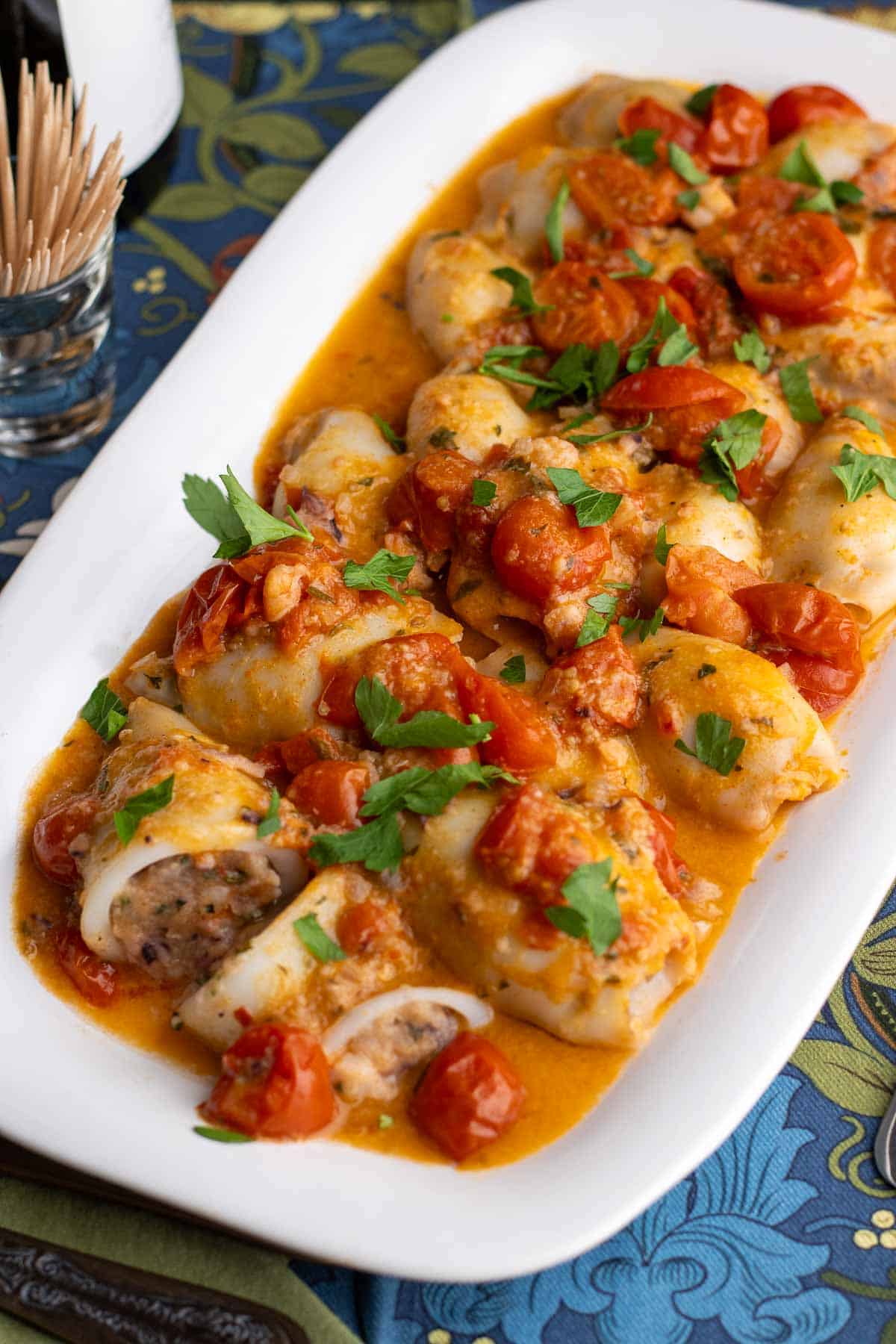 Stuffed calamari in tomatoes and white wine in a white serving dish.