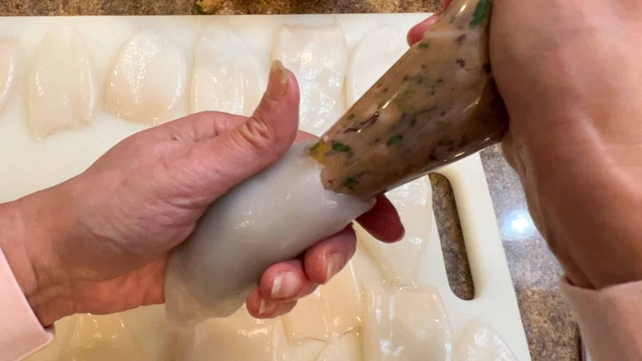 Filling a calamari body with a pastry bag filled with seafood stuffing.