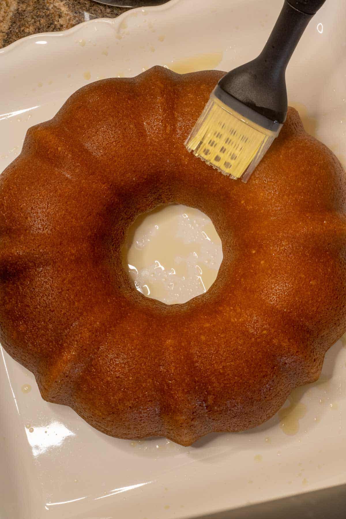 A Bundt cake on a square white dish being brushed with syrup.