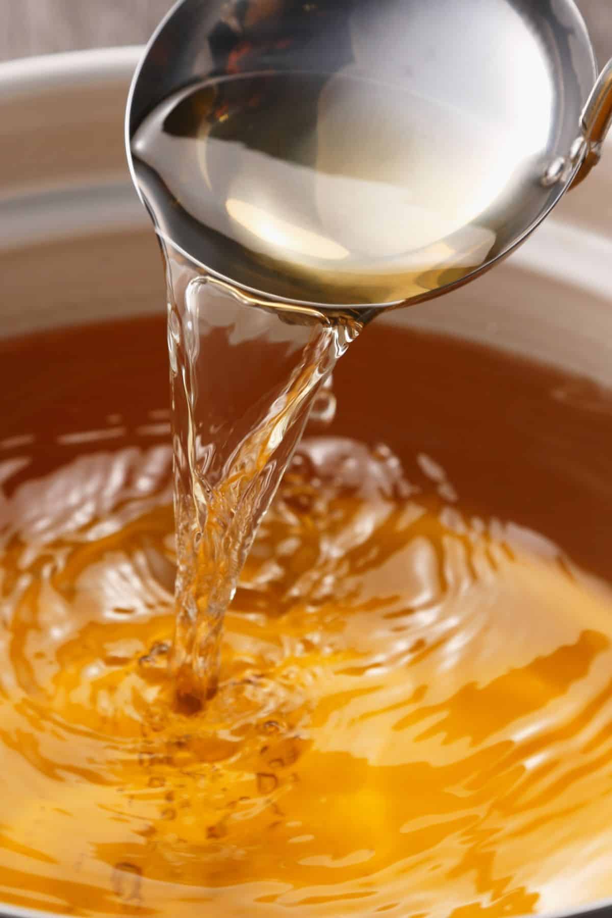 A ladle pouring syrup into a saucepan.