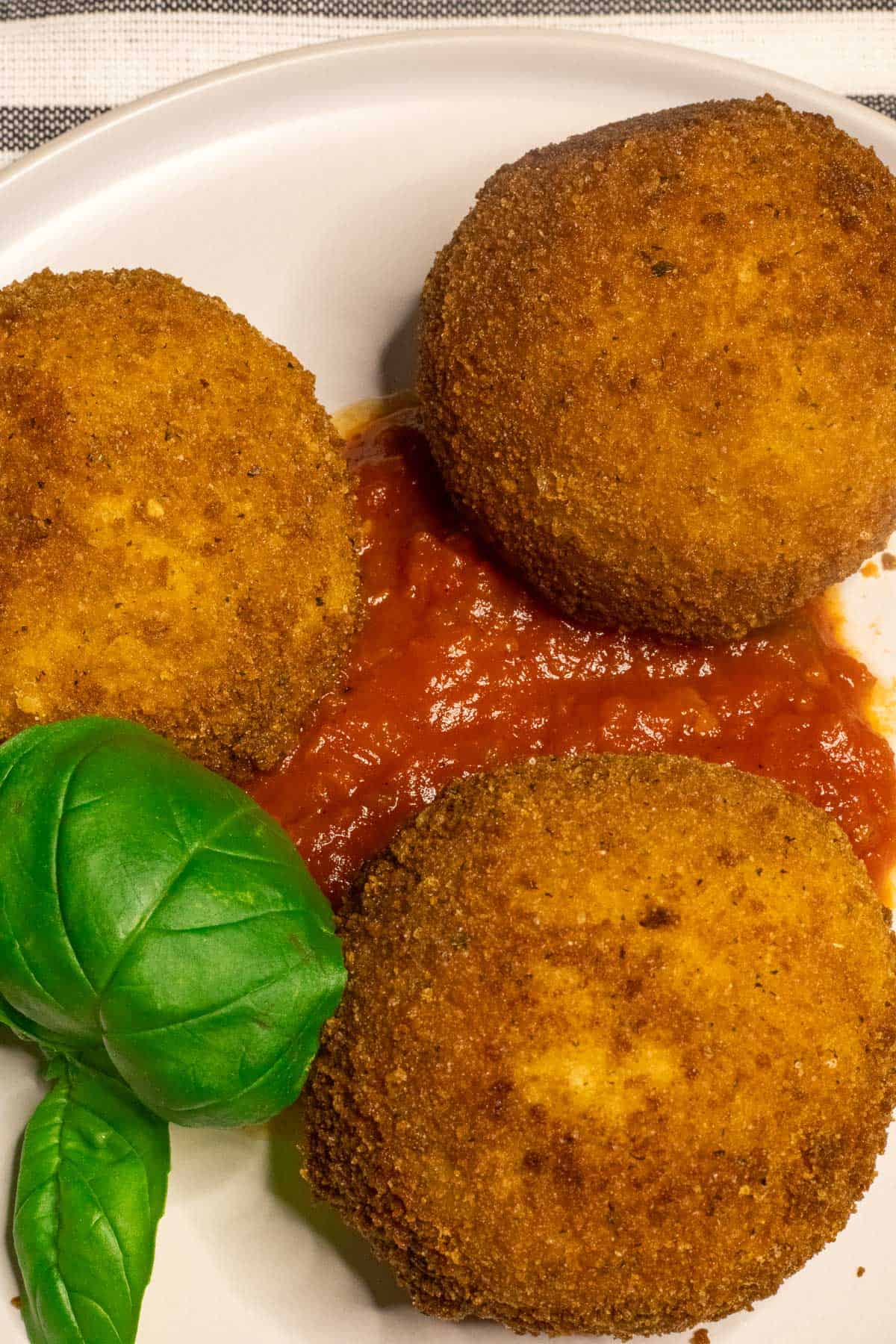Three arancini on a plate with tomato sauce.