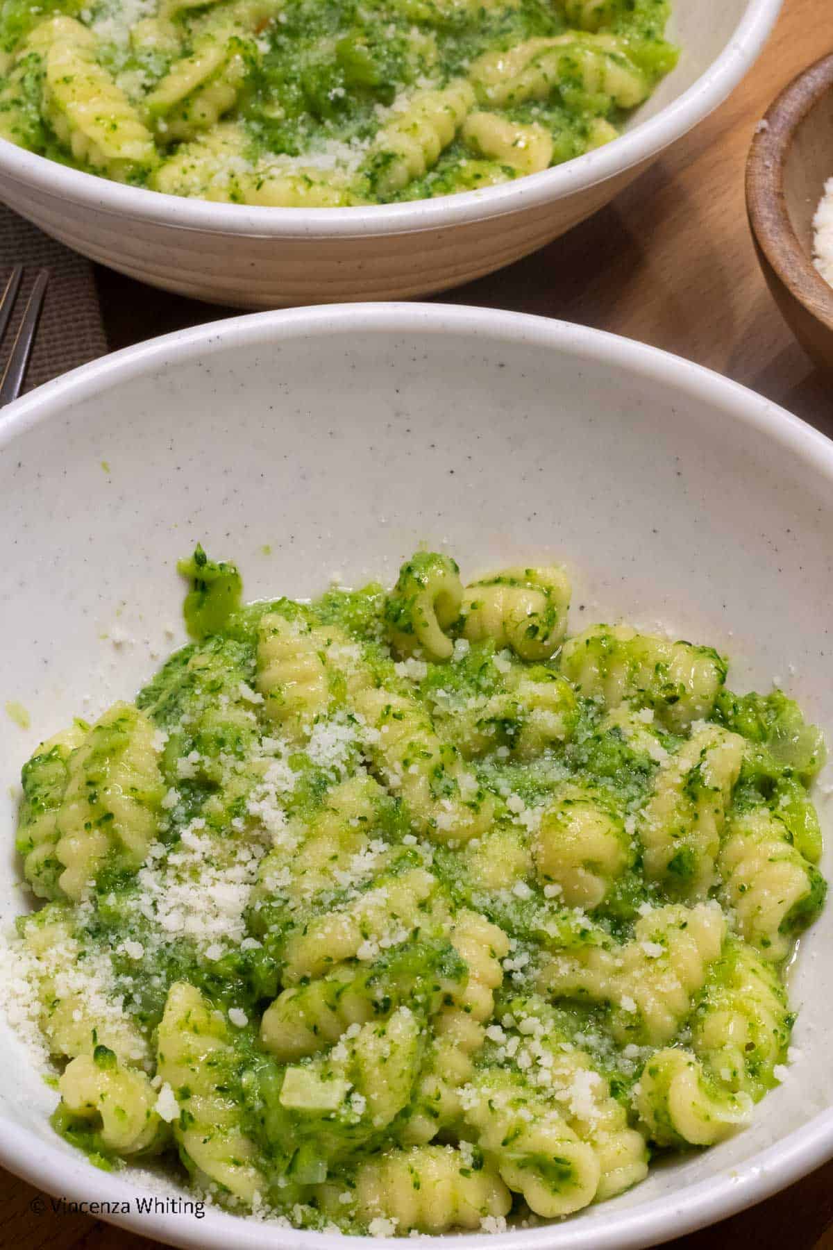 A bowl of shell shaped pasta with broccoli sauce and topped with grated cheese.