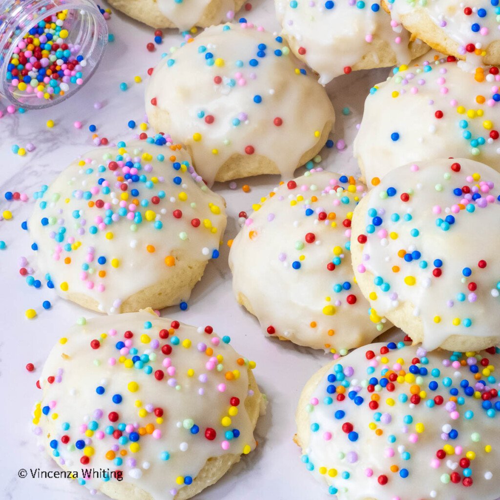 A pile of white drop cookies with white glaze frosting and colorful sprinkles.