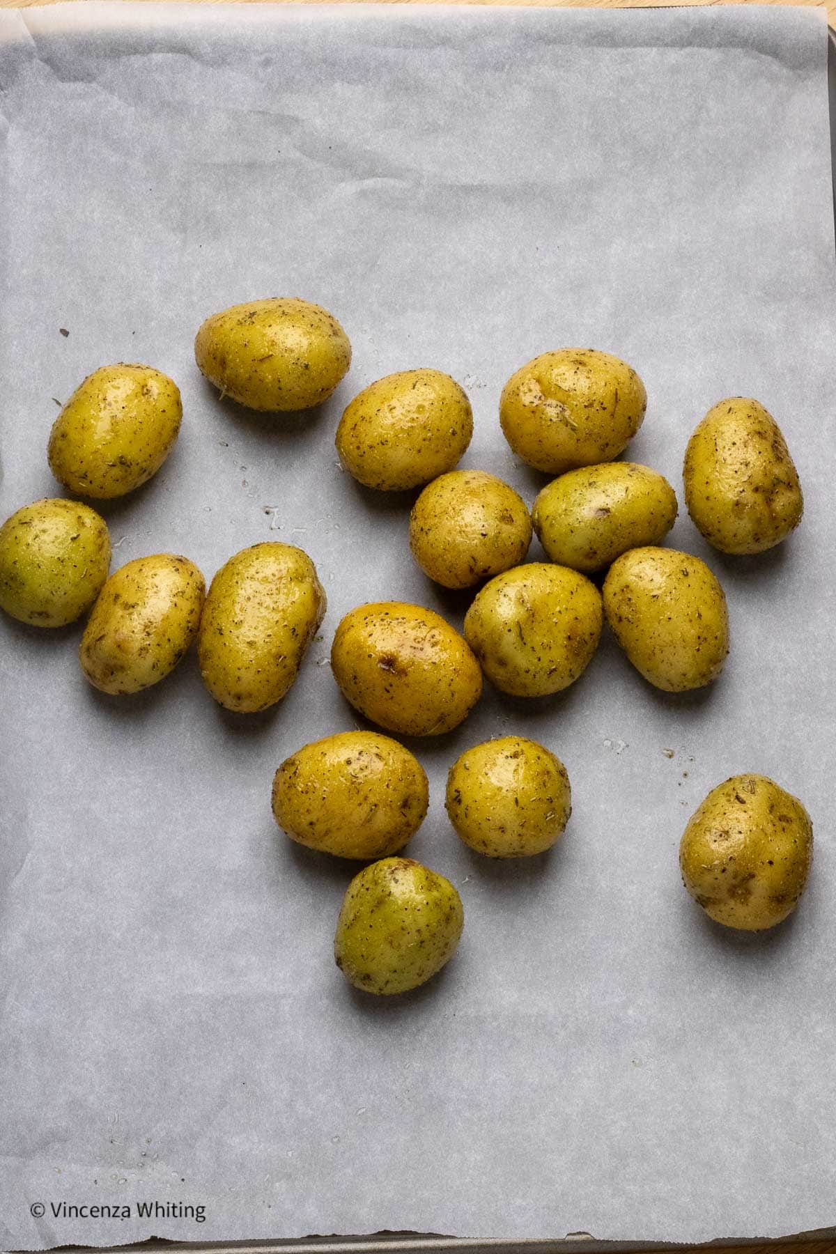 Seasoned baby potatoes on a parchment lined baking sheet.