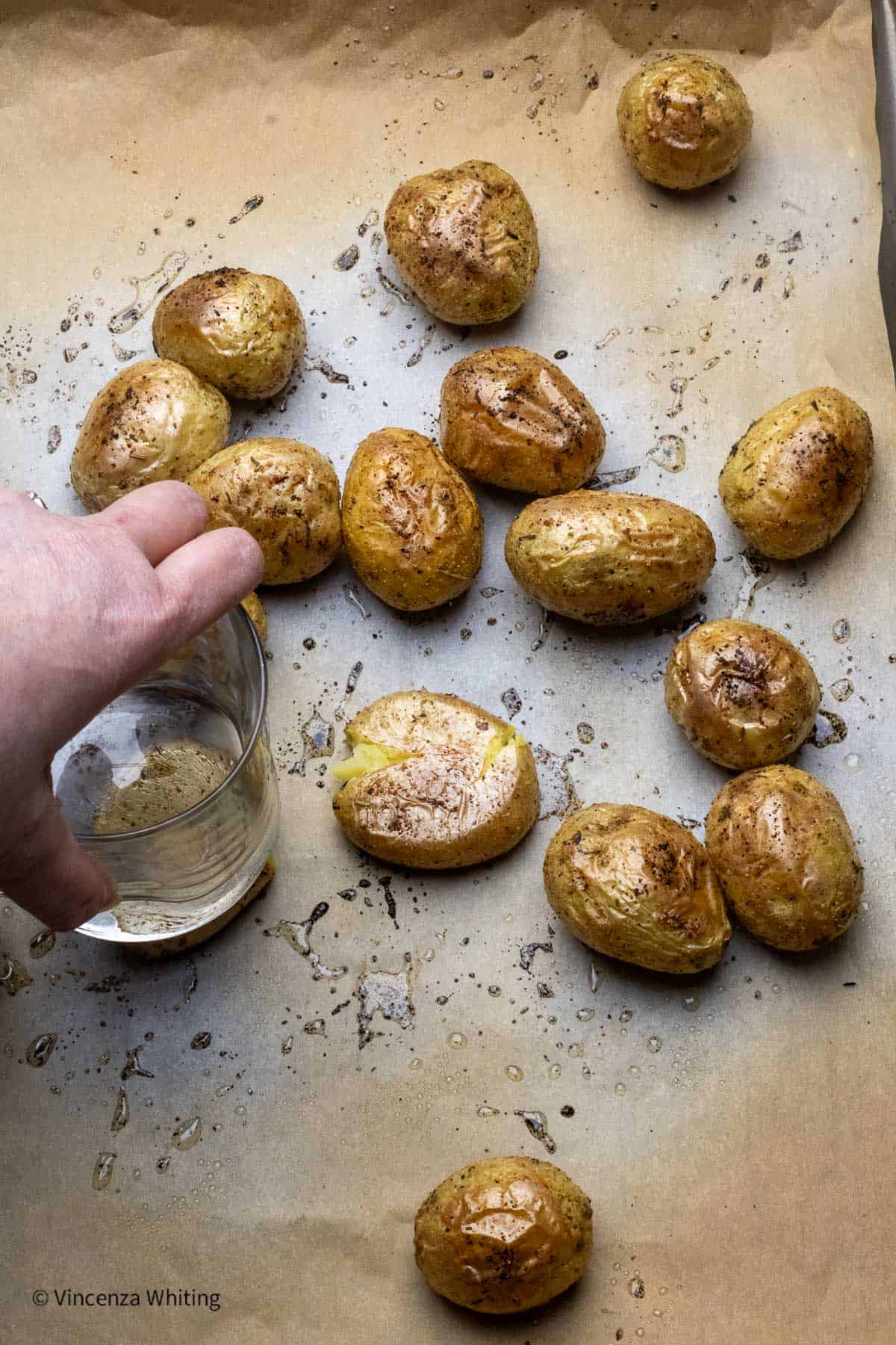 Roasted baby potatoes being smashed with the bottom of a glass.