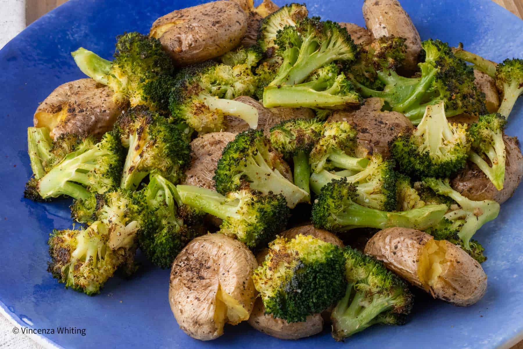 A blue bowl of roasted baby potatoes and broccoli.