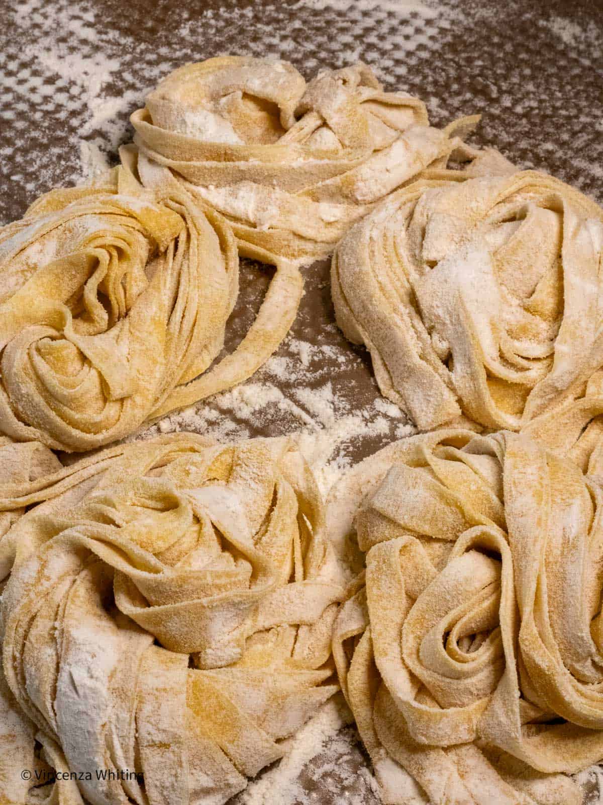 Fresh pasta nests dusted with flour on a baking sheet.