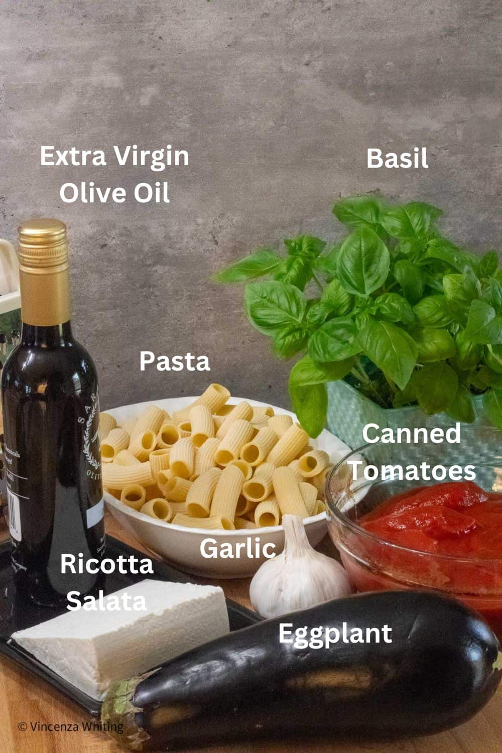 A photo of olive oil, cheese, basil, eggplant, a bowl of tomatoes, pasta and garlic.