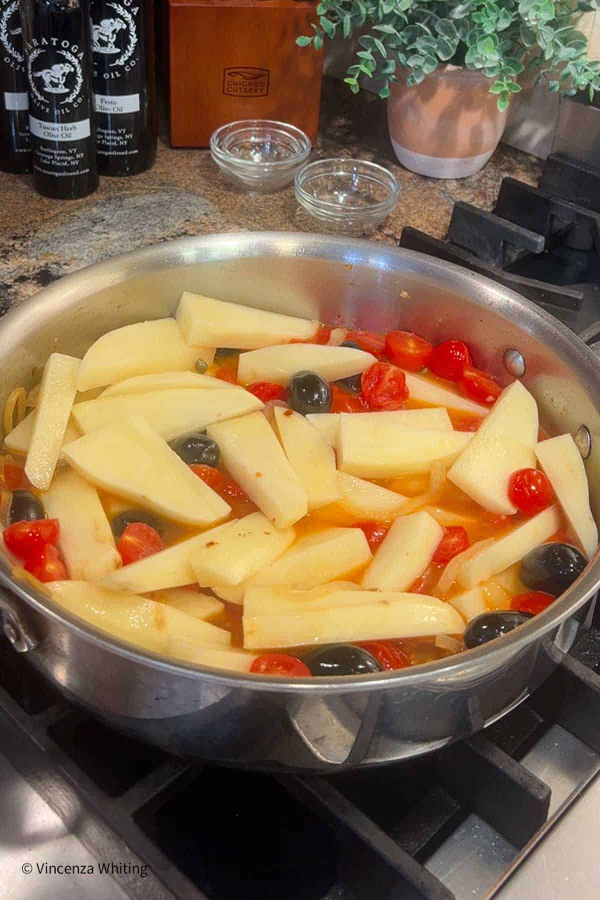 A sauté pan with tomatoes, potato slices and black olives