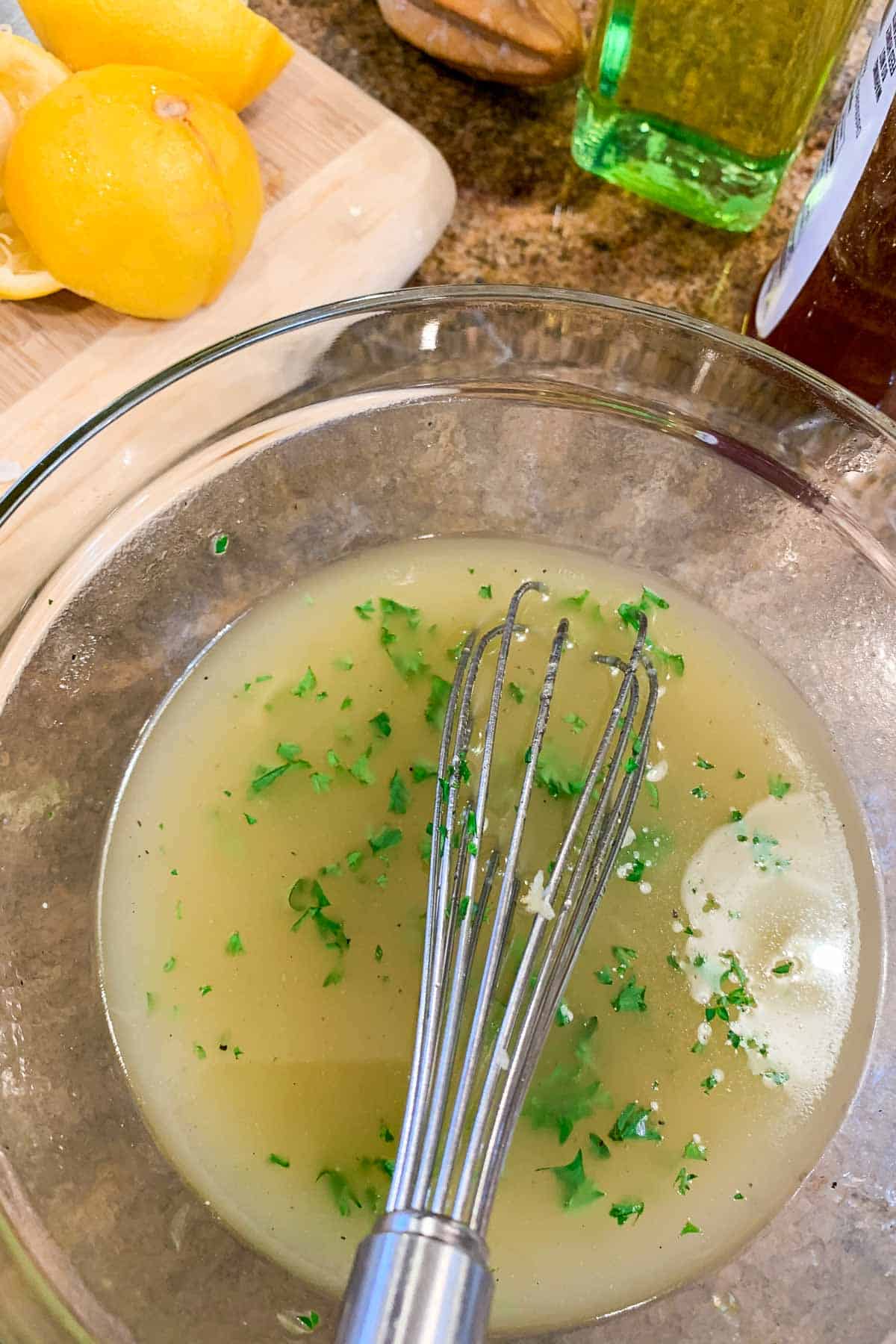 A bowl of lemon and garlic marinade with a wire whisk in it.