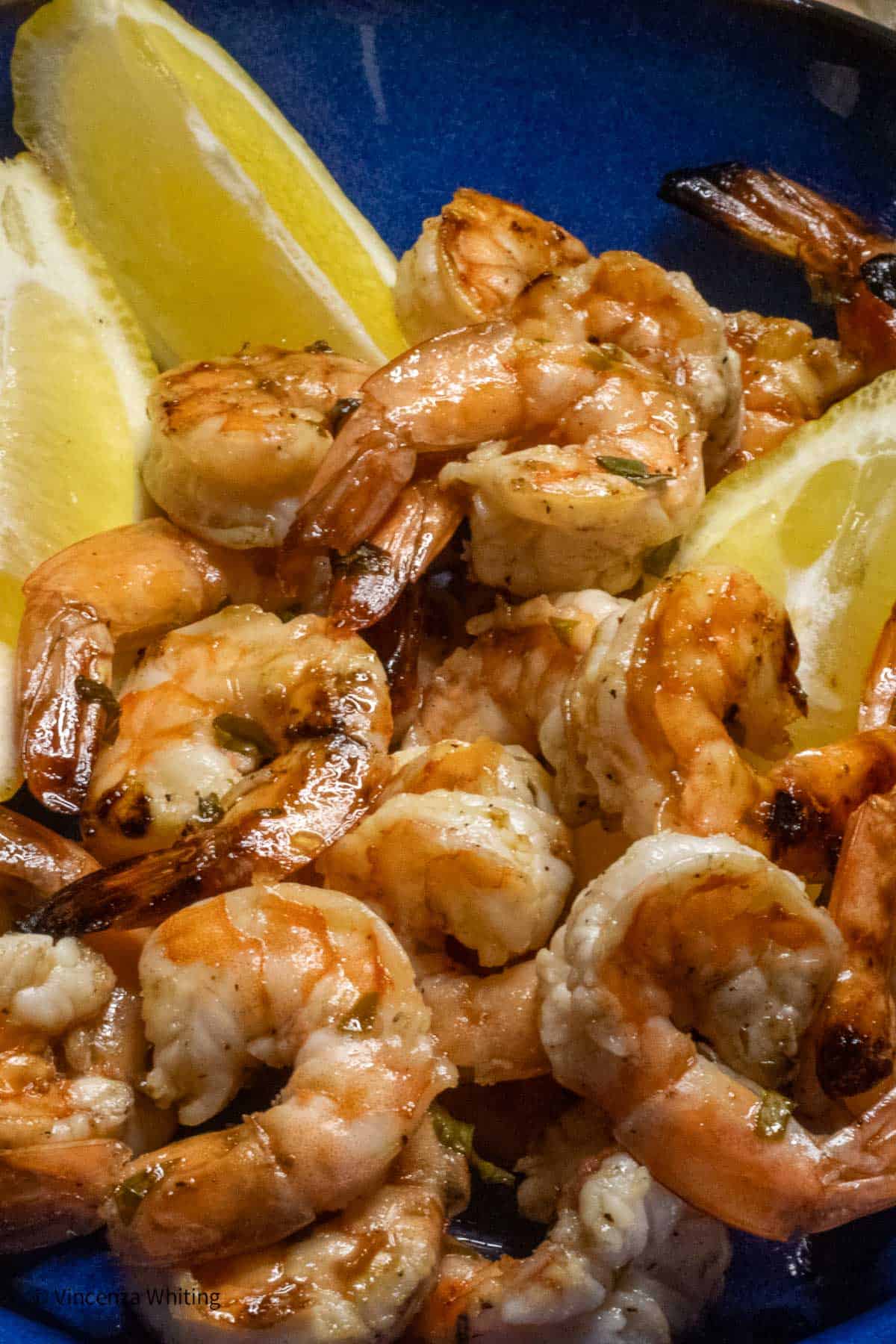 Grilled shrimp in a blue plate with lemon wedges.