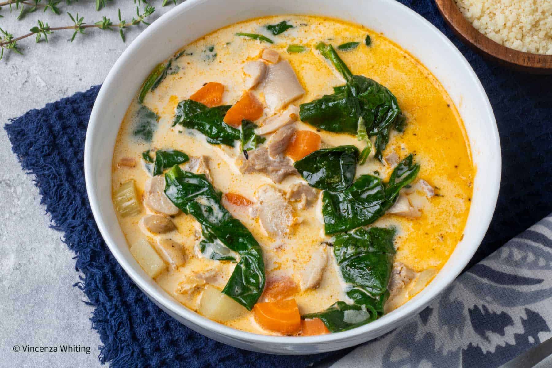 a bowl of cream chicken and vegetable soup on a blue cloth.