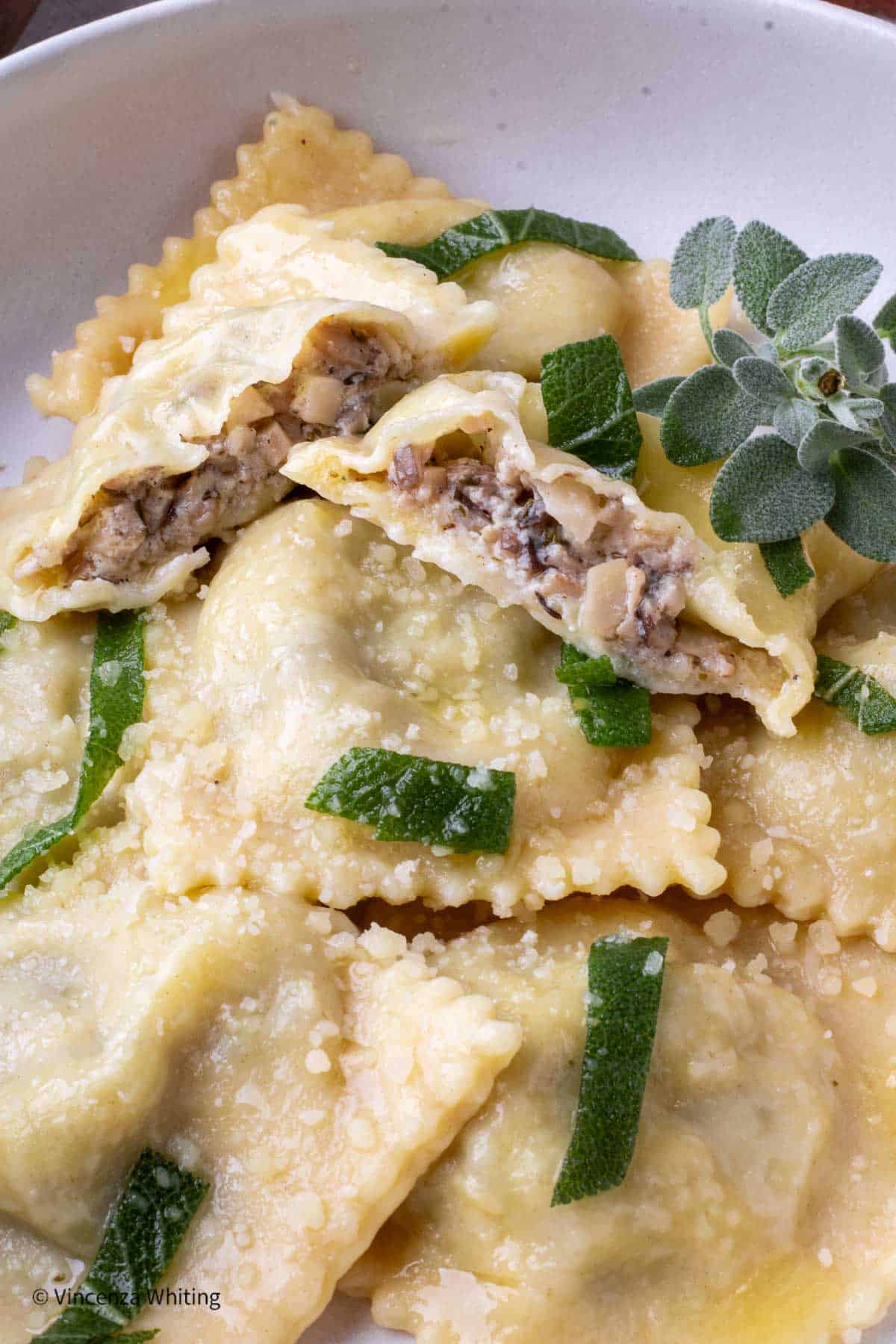 Mushroom filled ravioli in a white bowl with sage and parmesan cheese.