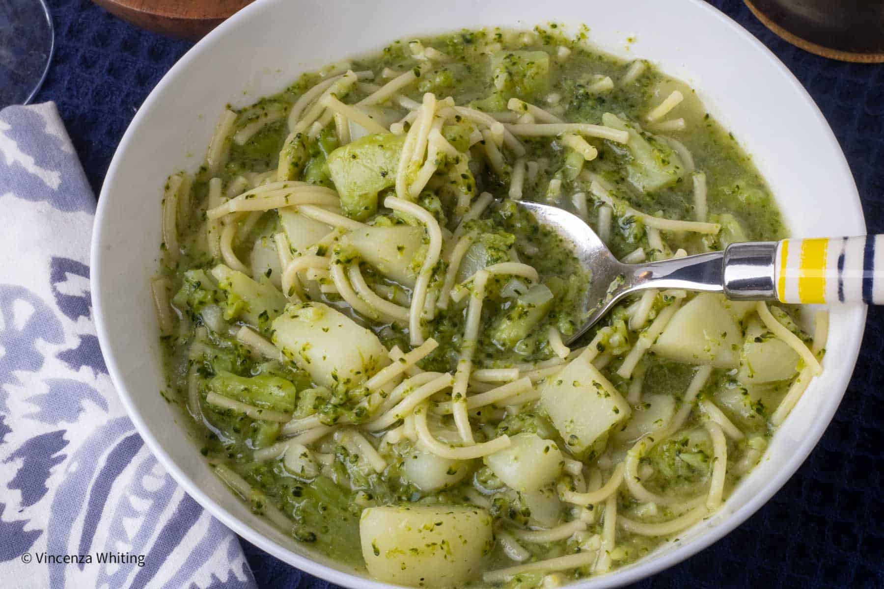 A bowl of broccoli and pasta soup with a spoon in it.