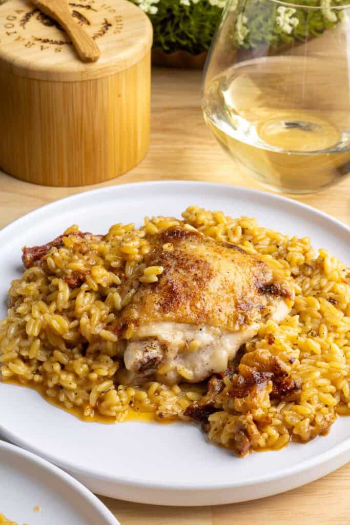 A white plate of chicken and orzo next to a glass of white wine.  