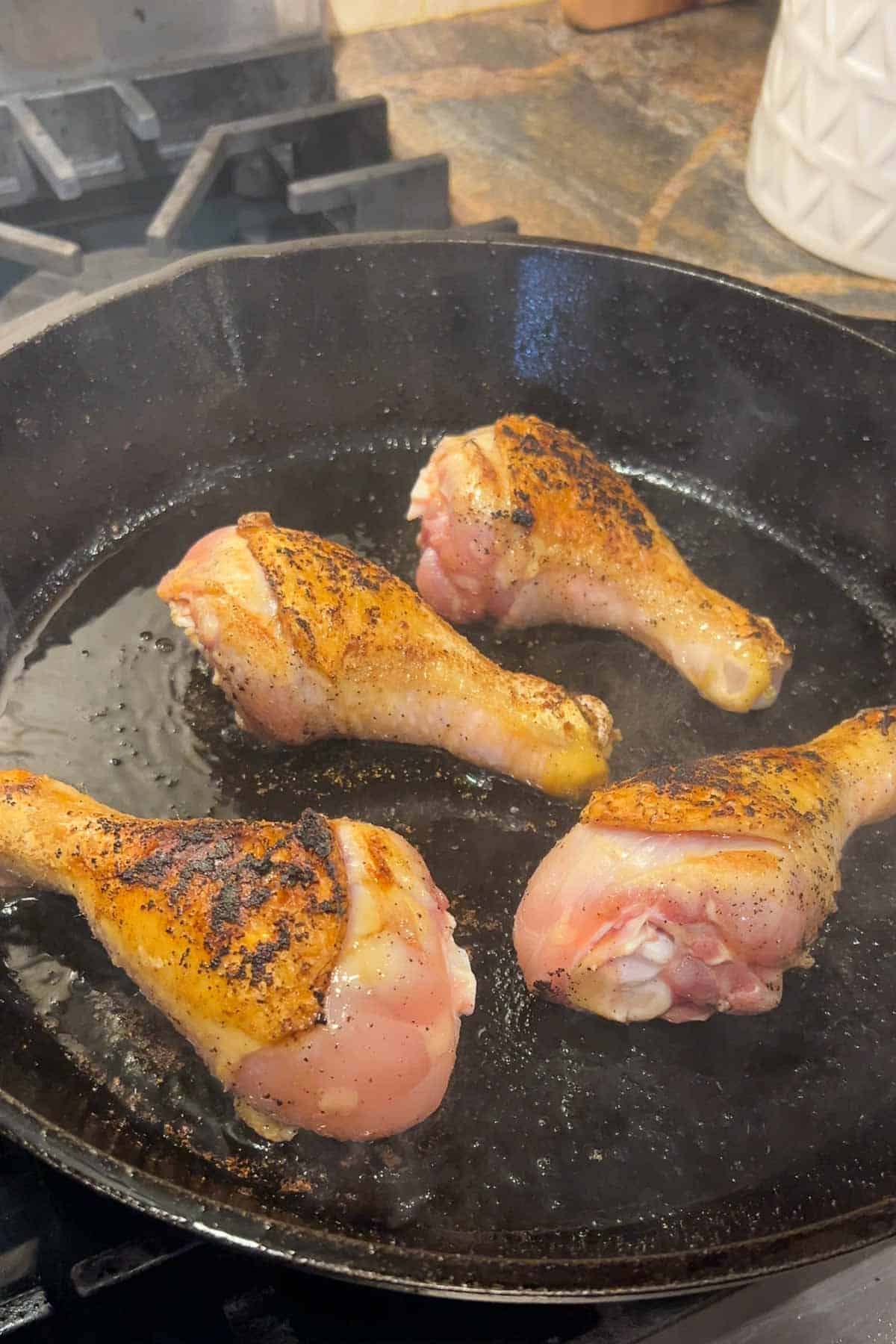 Chicken legs browning in a cast iron skillet.  