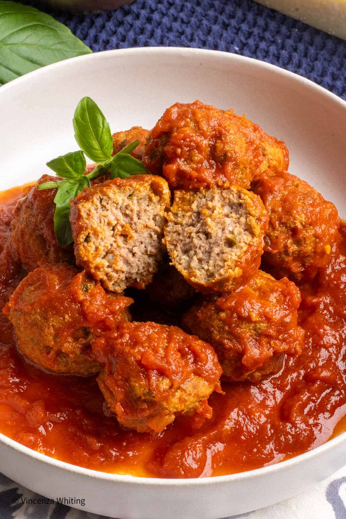 A mound of meatballs in a white bowl, and one is cut in half.