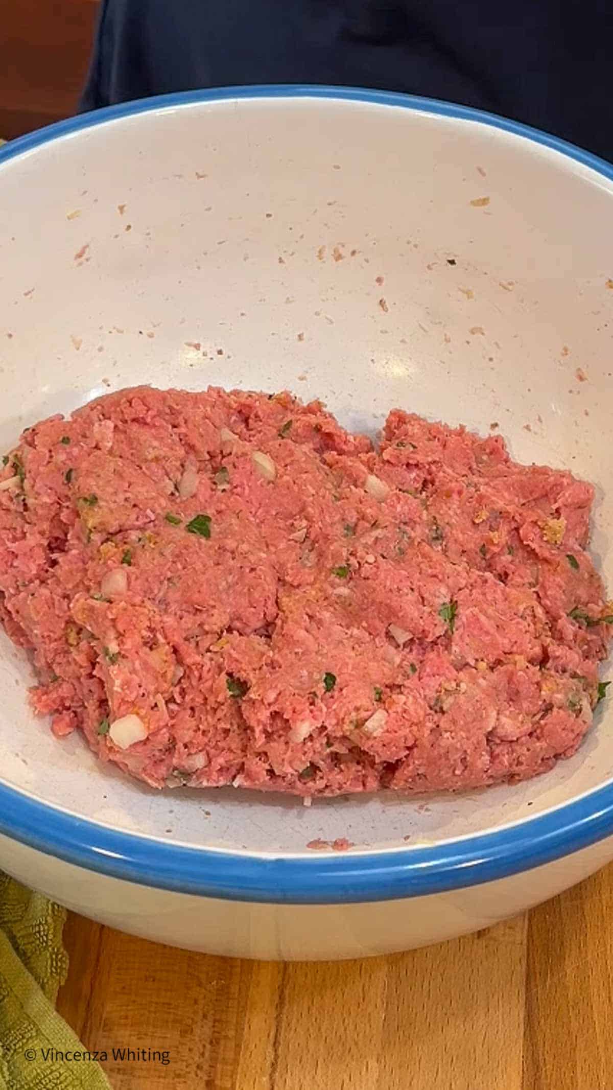 Meatball mixture in a white bowl with a blue rim.