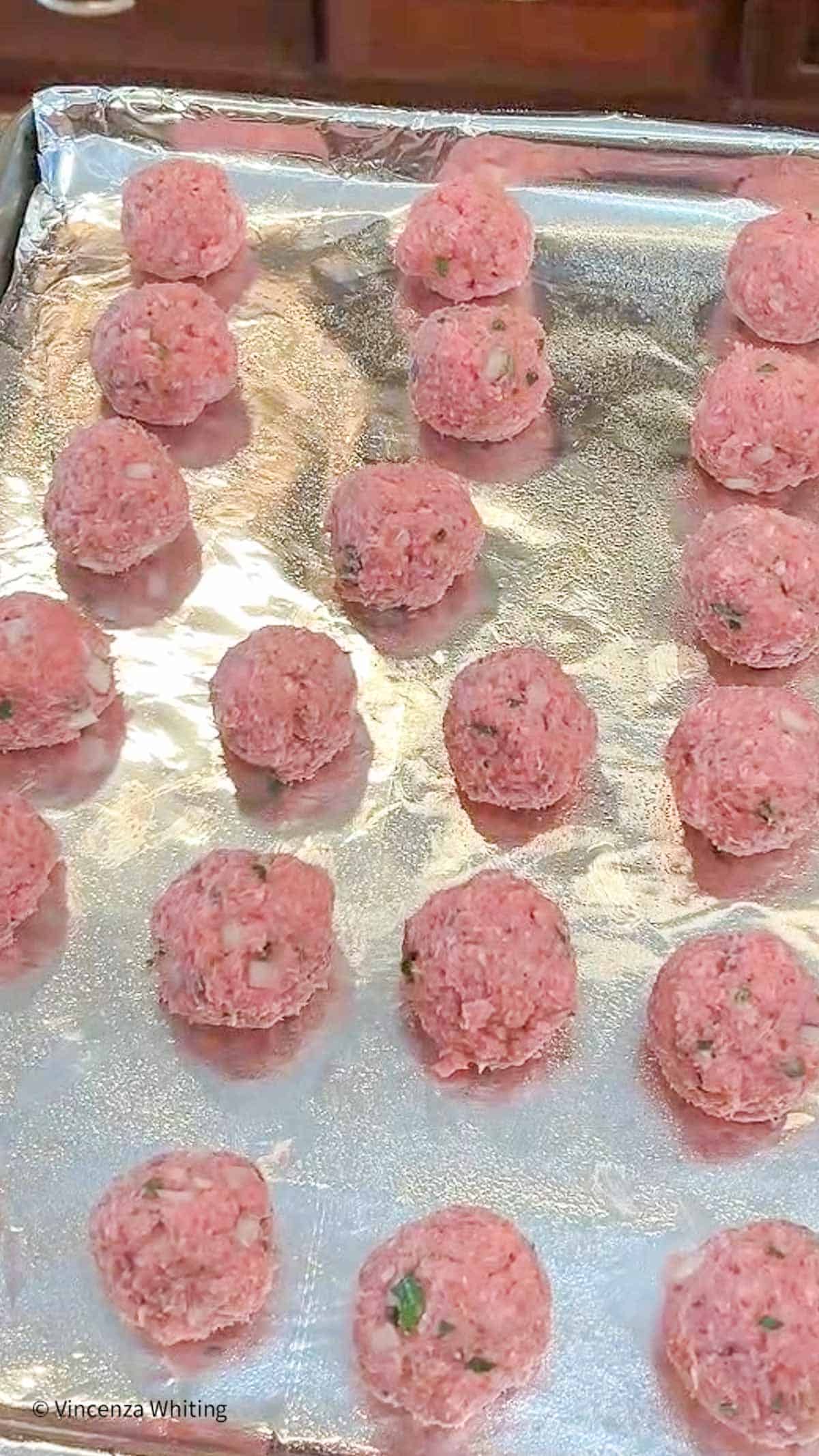 Raw meatballs on foil-lined baking sheet.