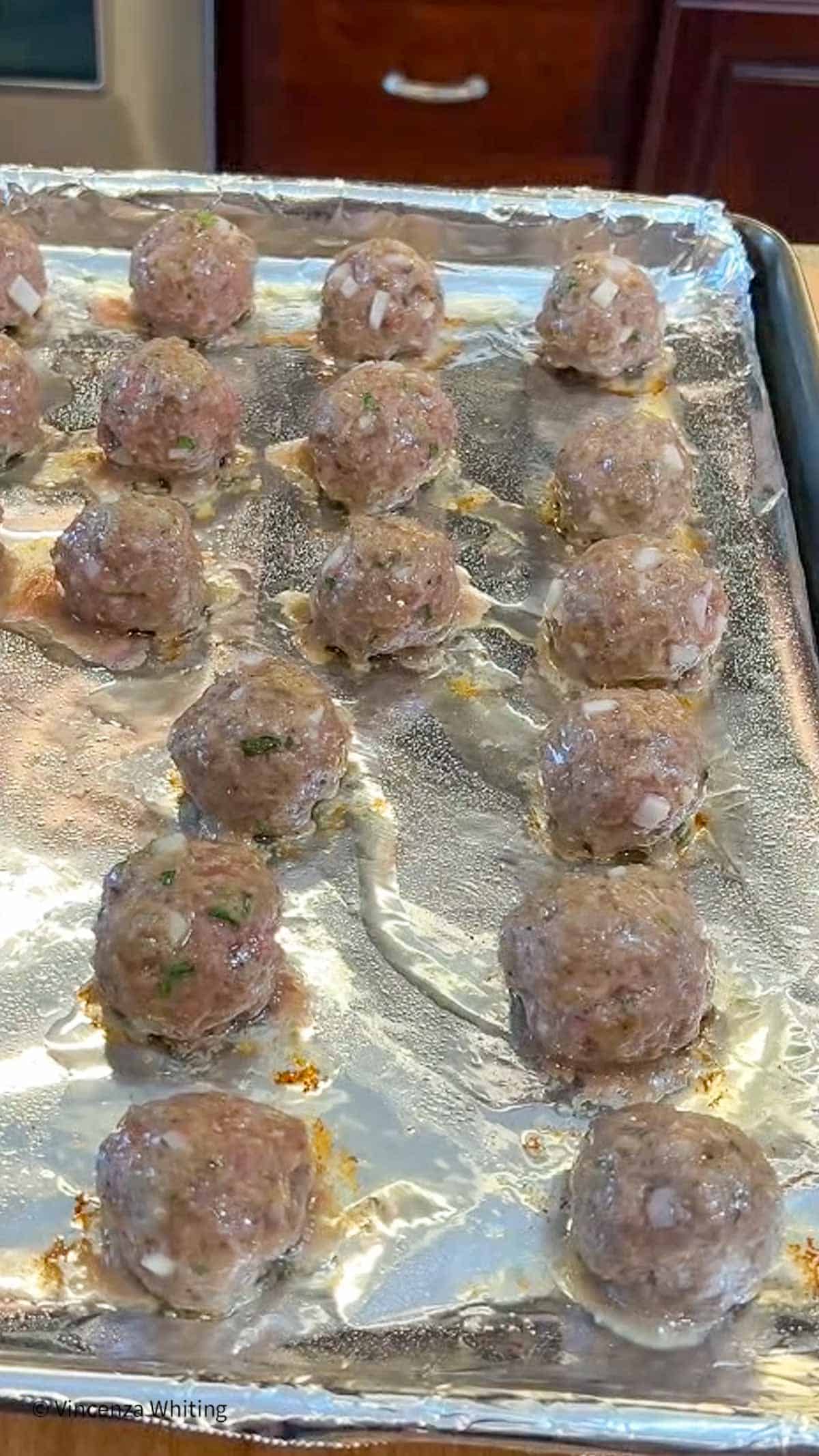 Partially cooked meatballs on a foil-lined baking sheet.