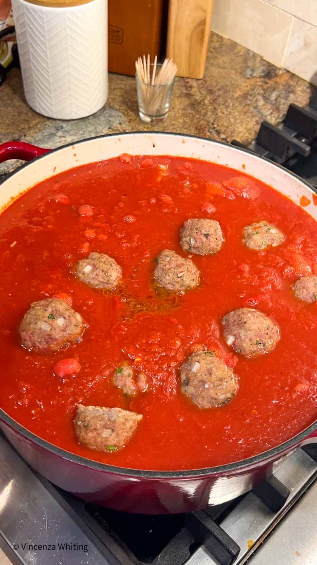 Meatballs are added to a pot of tomato sauce.