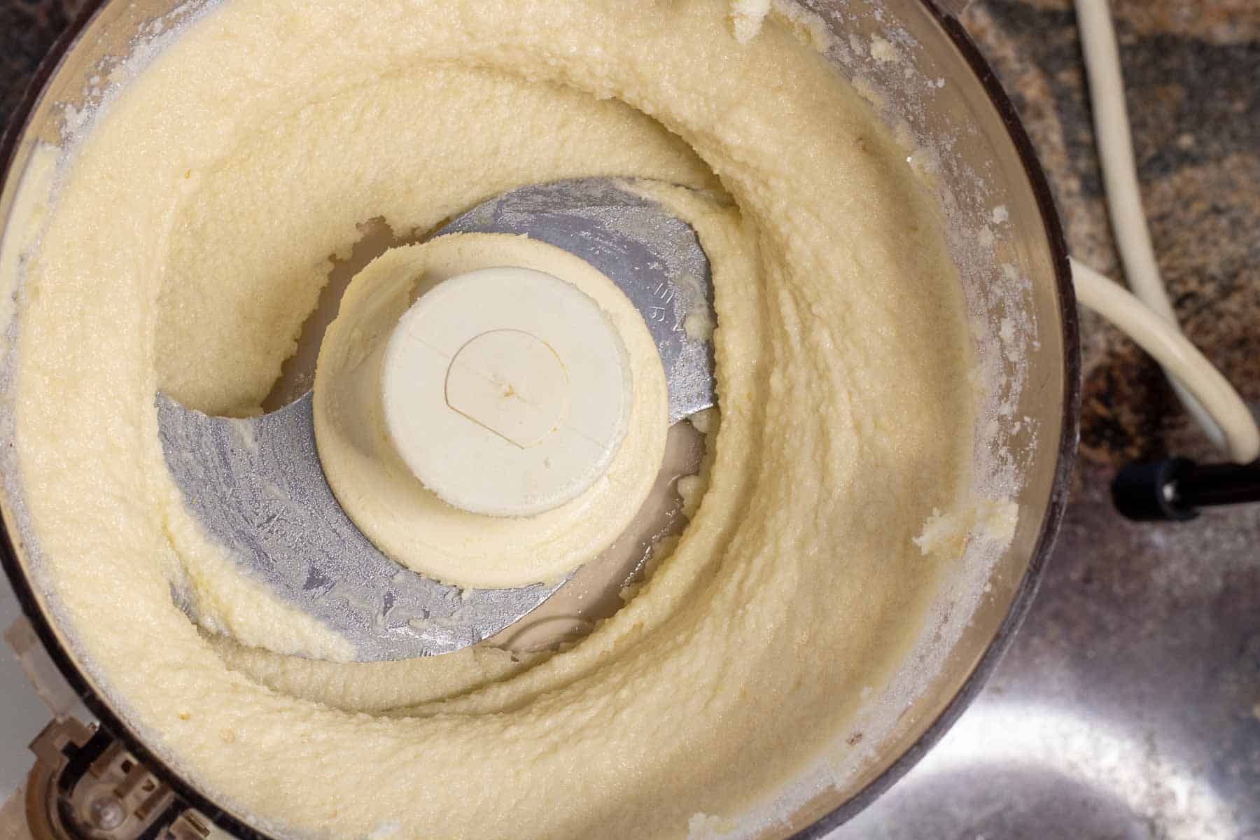 A creamy mixture of butter, almond paste and sugar in the bowl of a food processor.