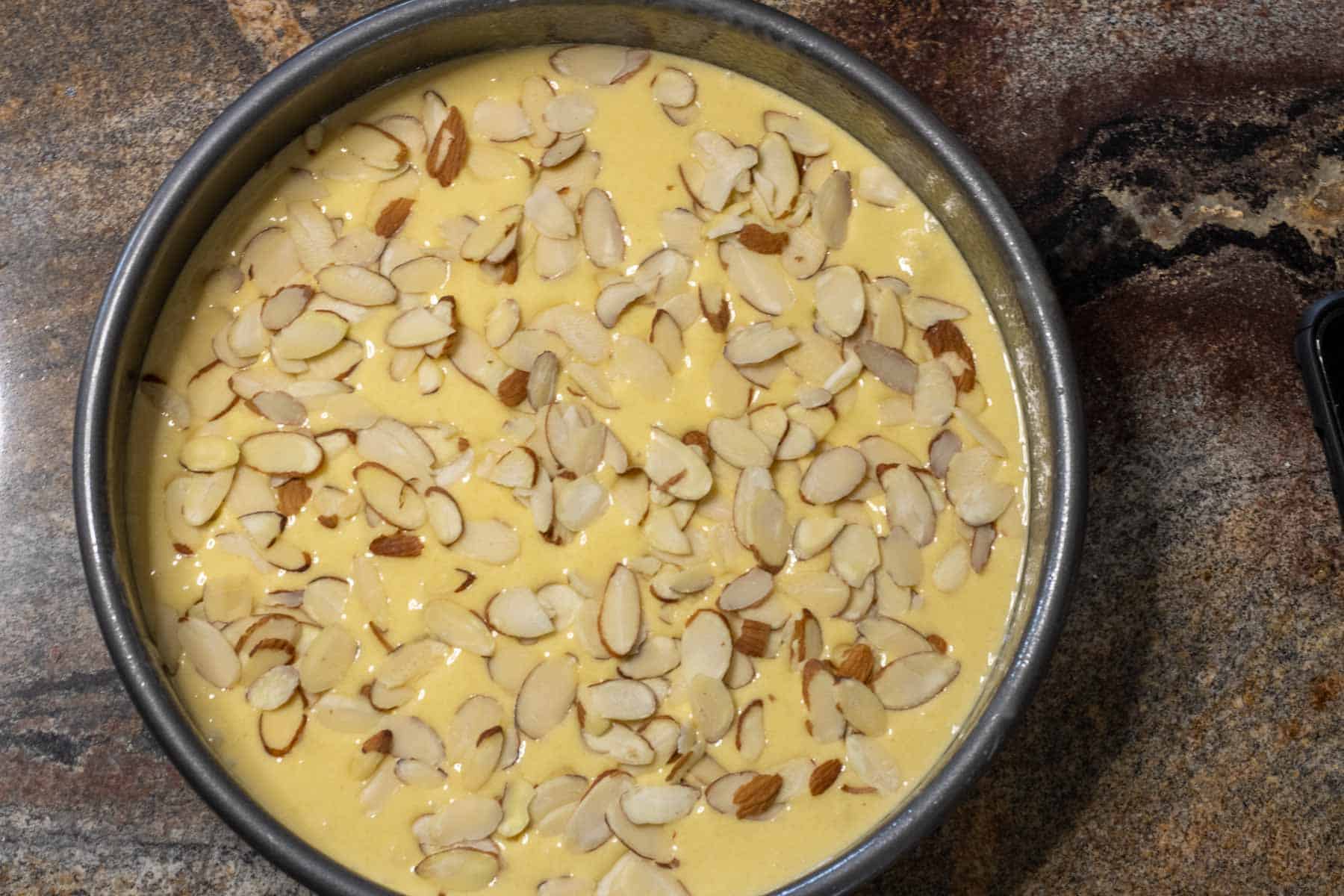 Cake batter in a round baking pan sprinkled with sliced almonds.