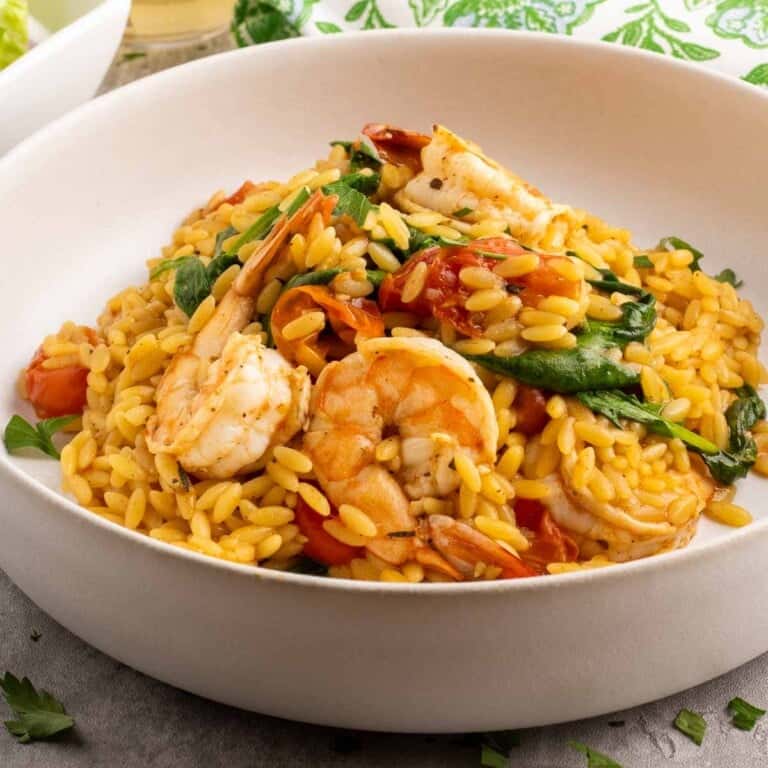 Shrimp and Orzo pasta with tomatoes and spiniach in a white bowl.