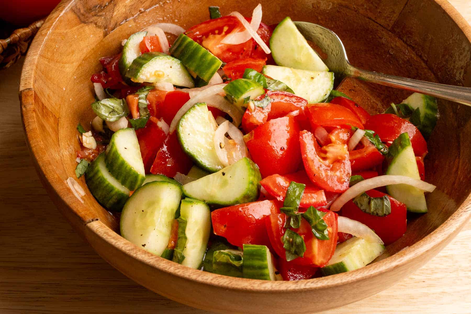 A close up photo of a wood bowl filled with Mediterranean Tomato and Cucumber salad.