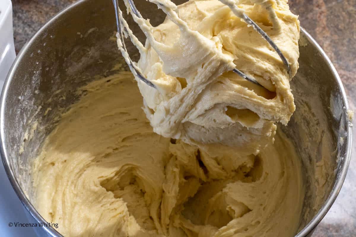 A beater filled with cookie dough over a bowl of cookie dough.