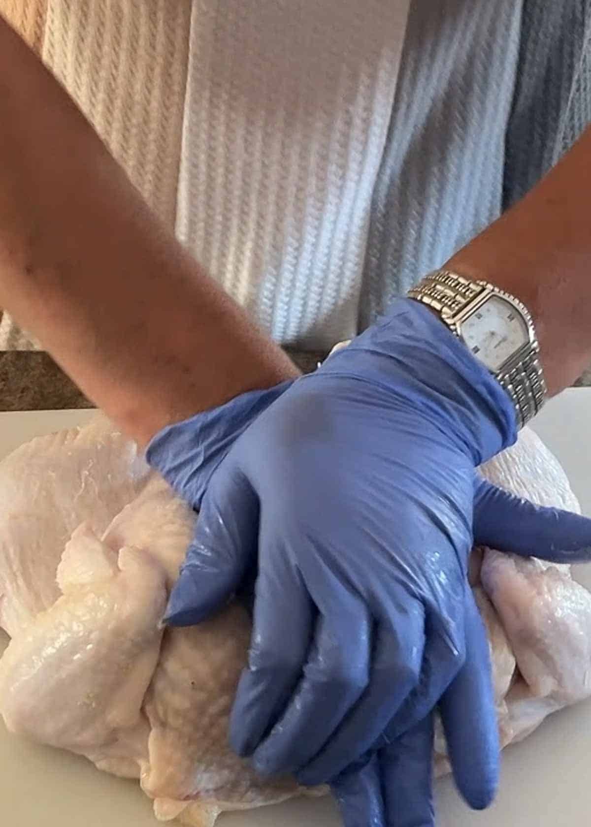 Hands are pressing down on a whole chicken, that has had the breastbone removed to prepare it for roasting. 
