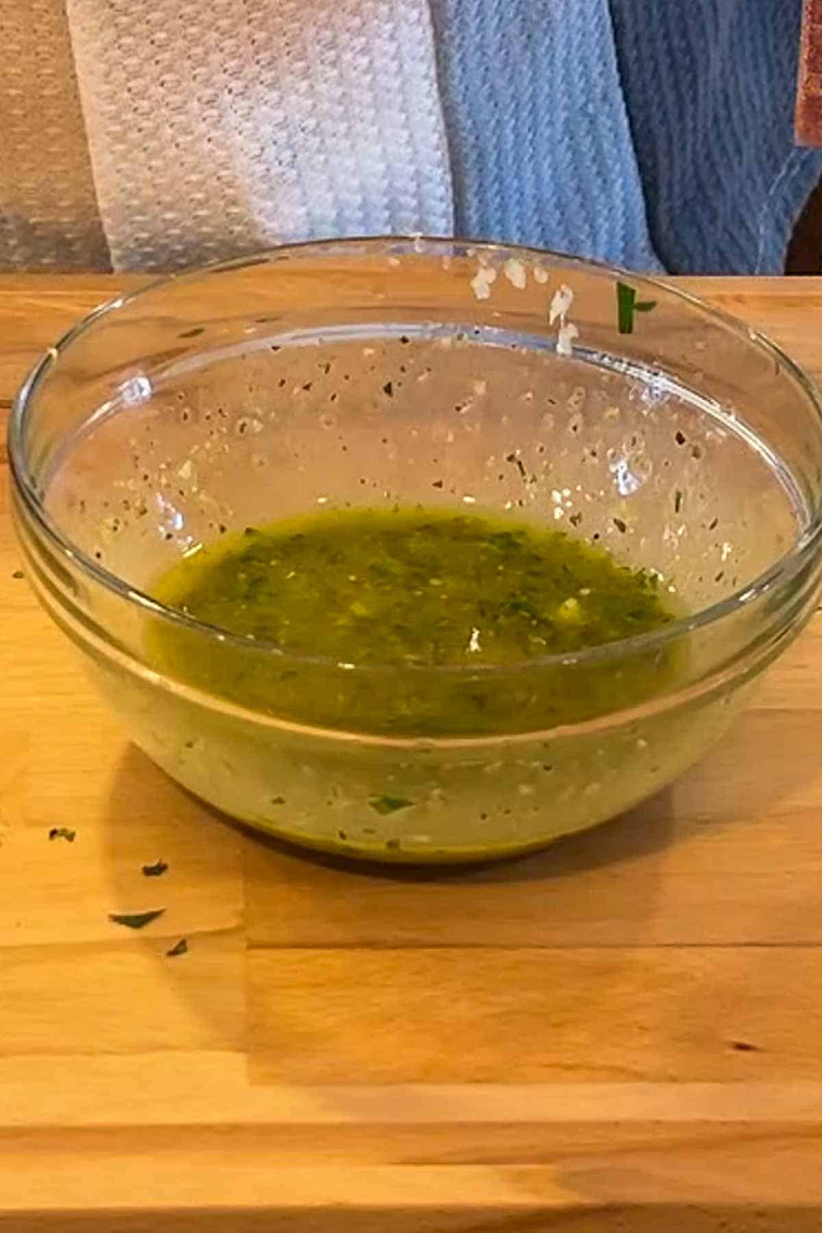 A bowl of Salmoriglio sauce on a lcutting board.