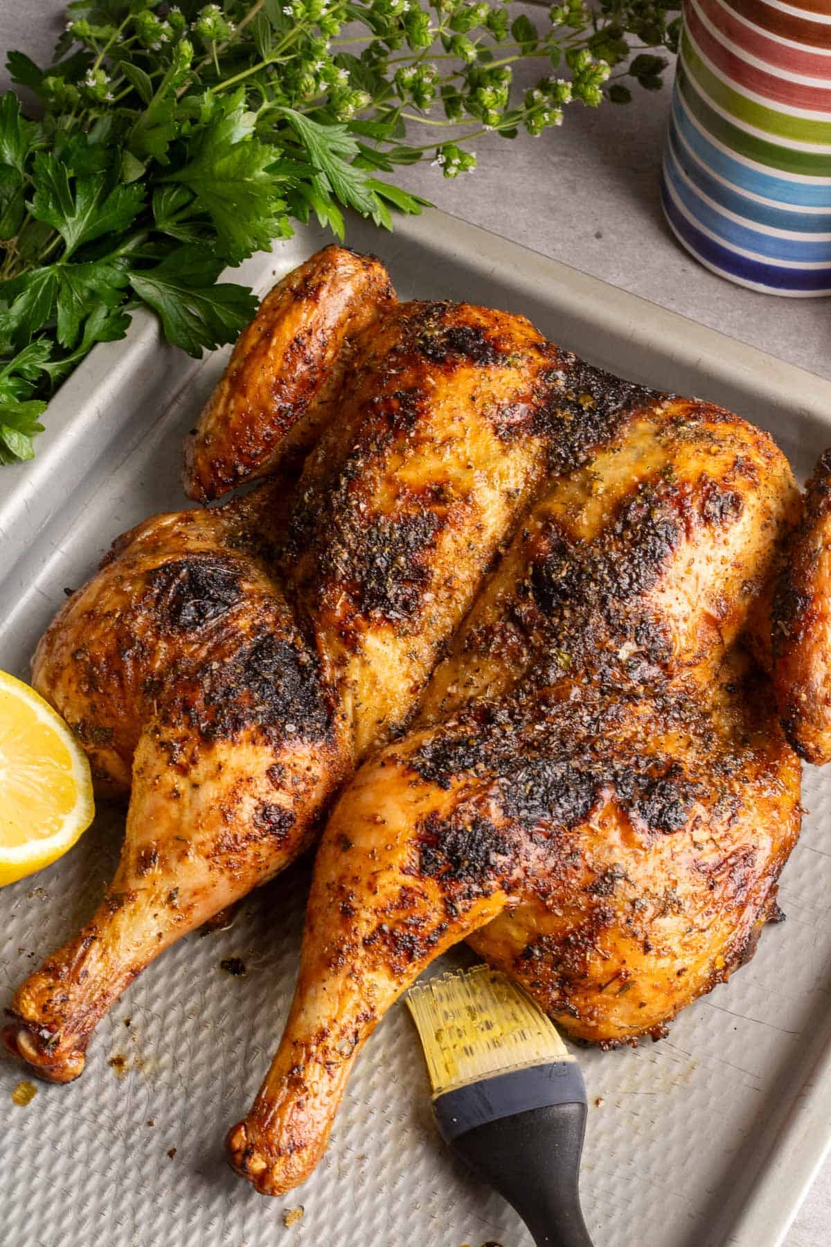 A whole grilled chicken on a metal sheet pan with a basting brush.