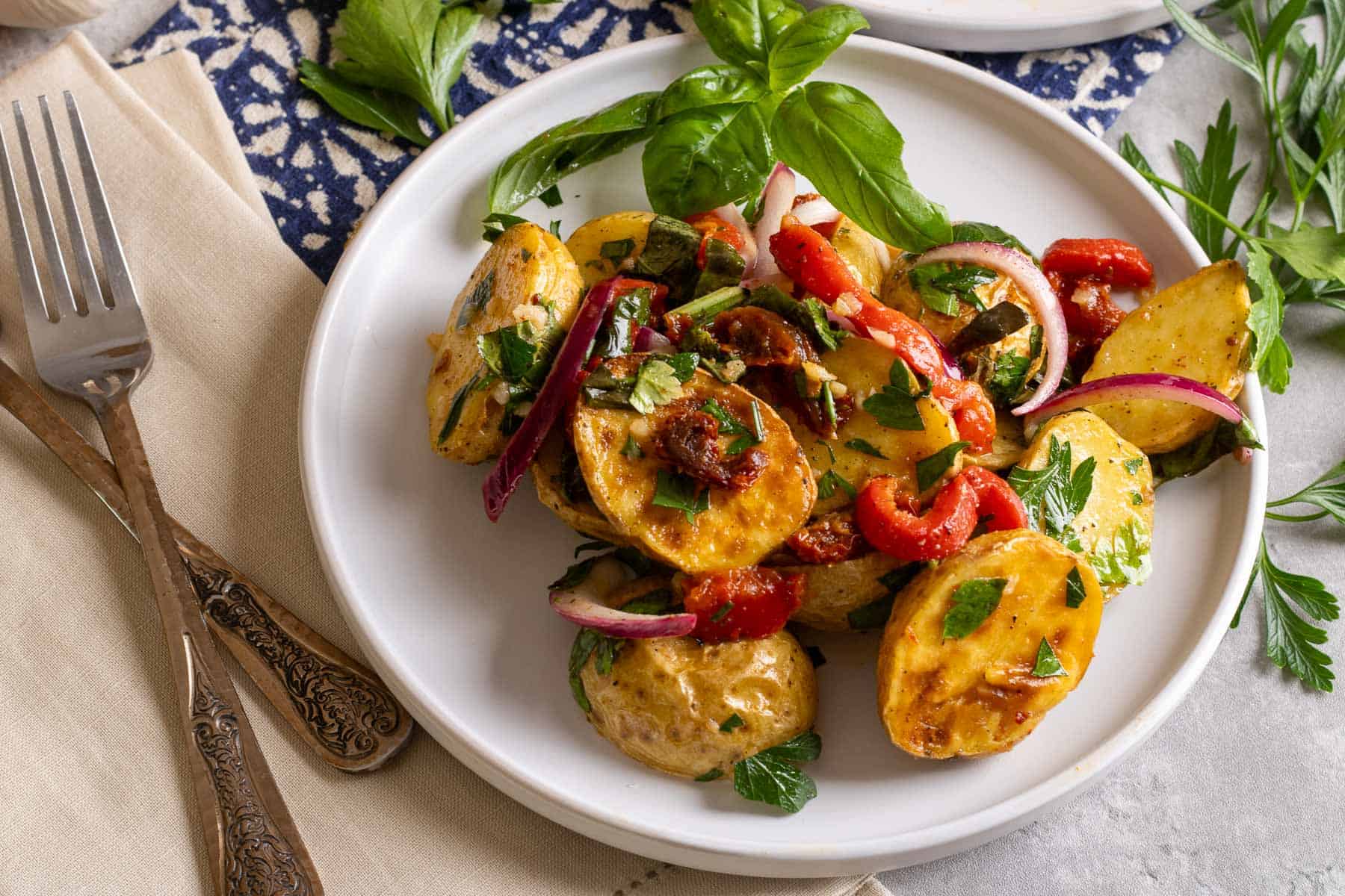A white plate of roasted potato salad next to a tan napkin with two forks.