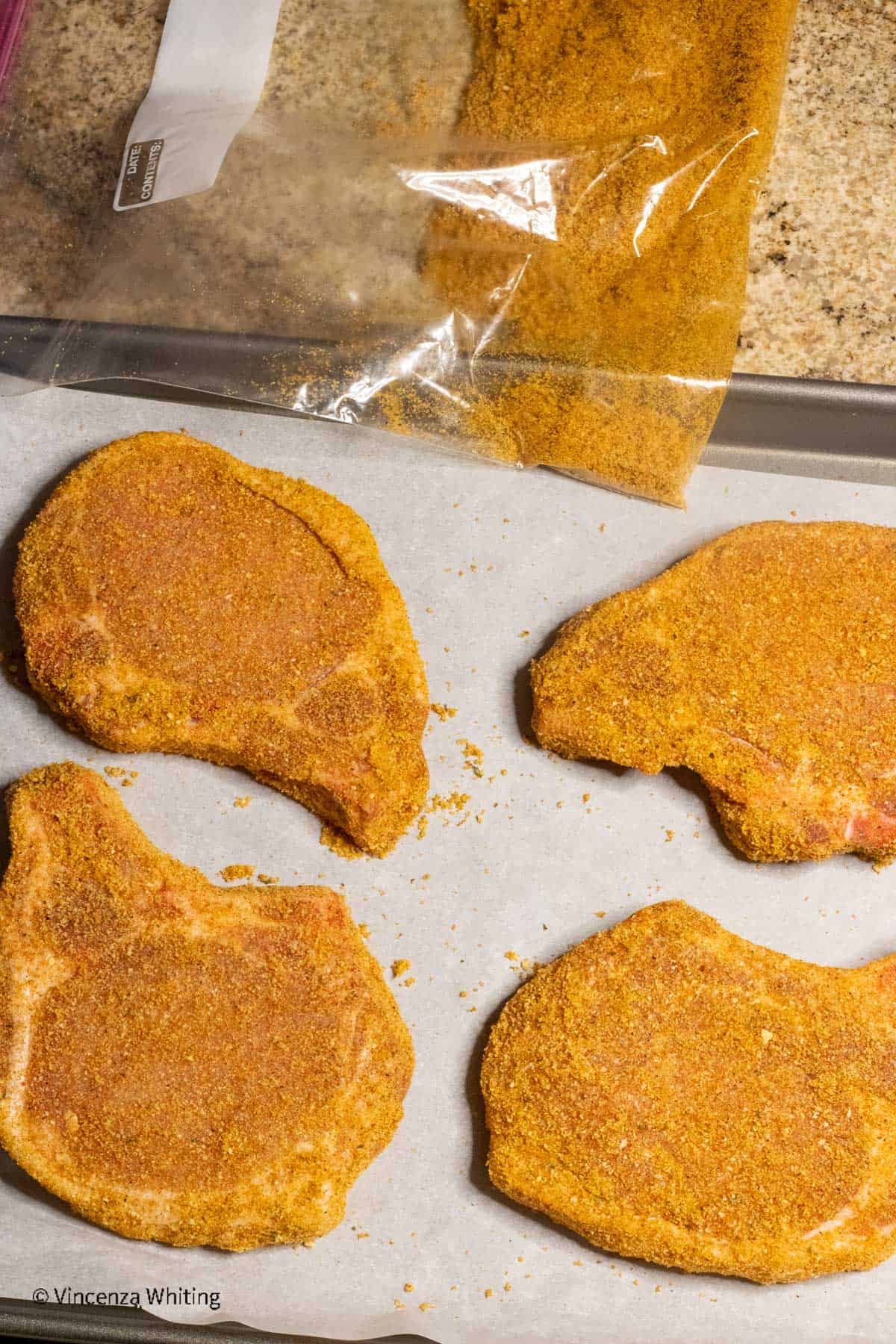 Four breaded pork chops on a baking sheet lined with parchment paper.