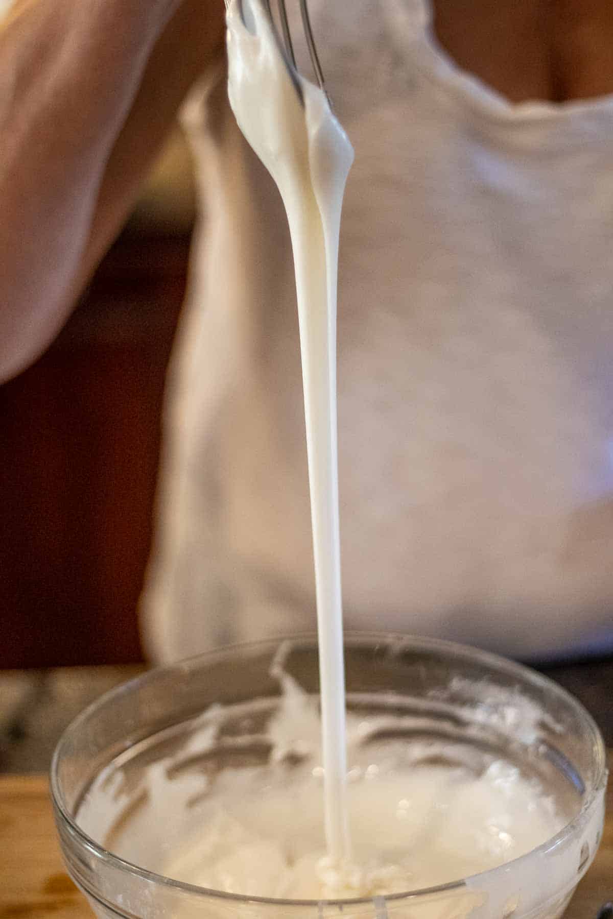 A white frosting is being dripped off of a whisk into a bowl.