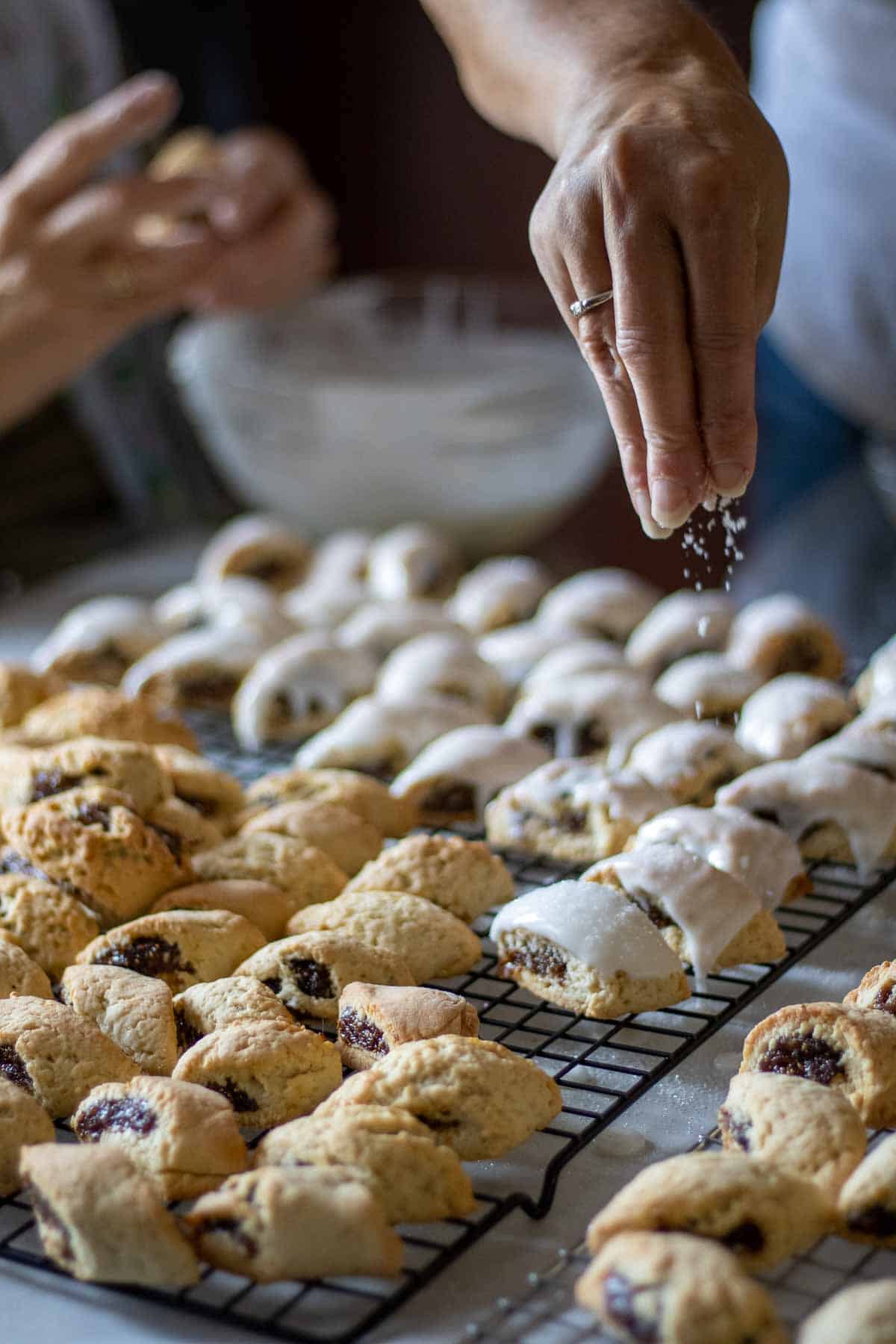 Cookies on a drying rack being frosted and decorated with sanding sugar.